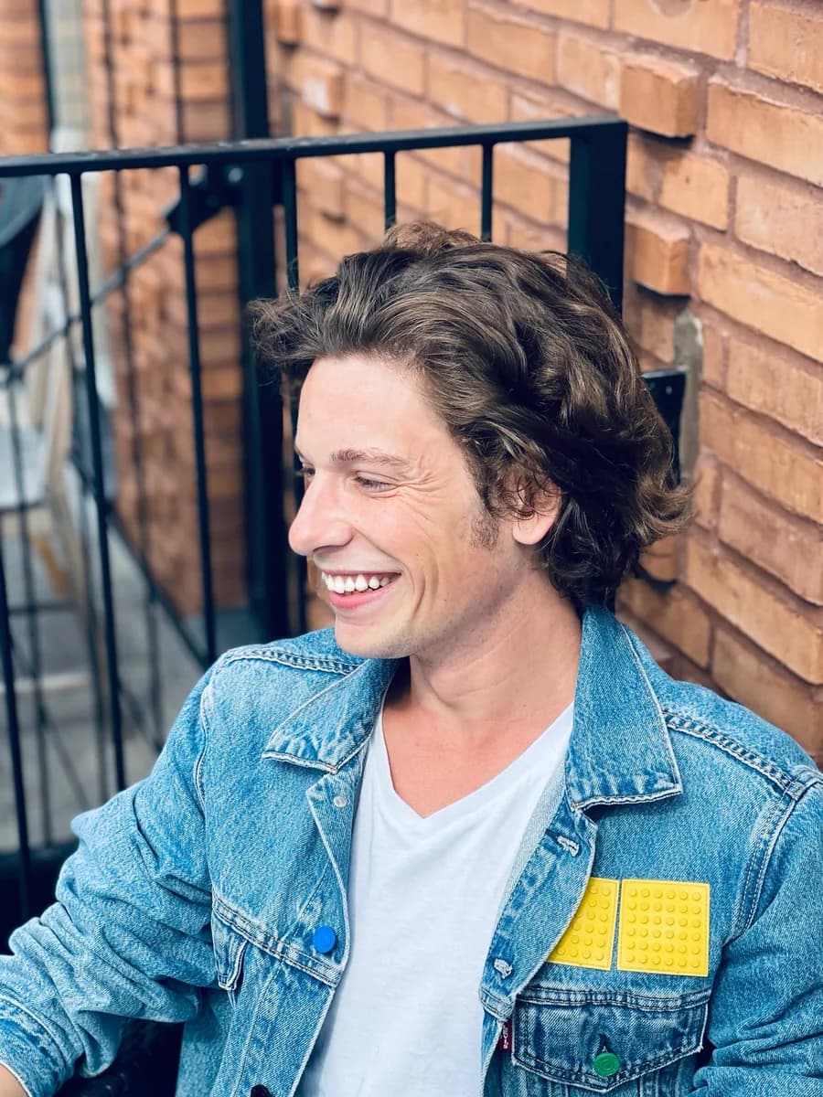 Mathieu, souriant, veste en jean devant un mur de briques